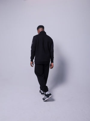 4GAINS Tracksuit Hose in der Farbe schwarz mit schwarzem Puff Print an einem stehenden männlichem Model