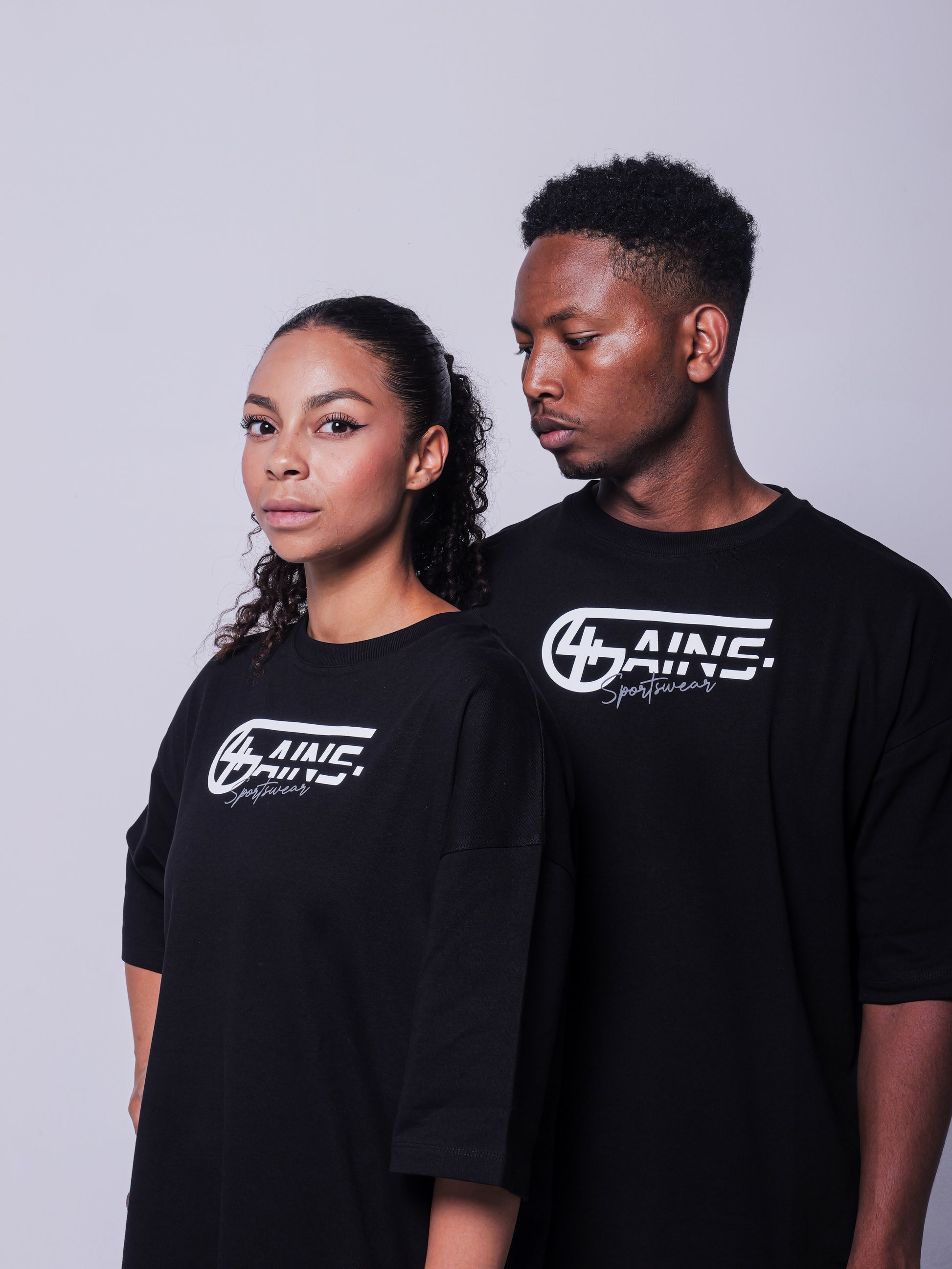 4GAINS Sportswear oversized T-shirt in der Farbe schwarz mit weißem Aufdruck an einem weiblichen und männlichen Model stehend