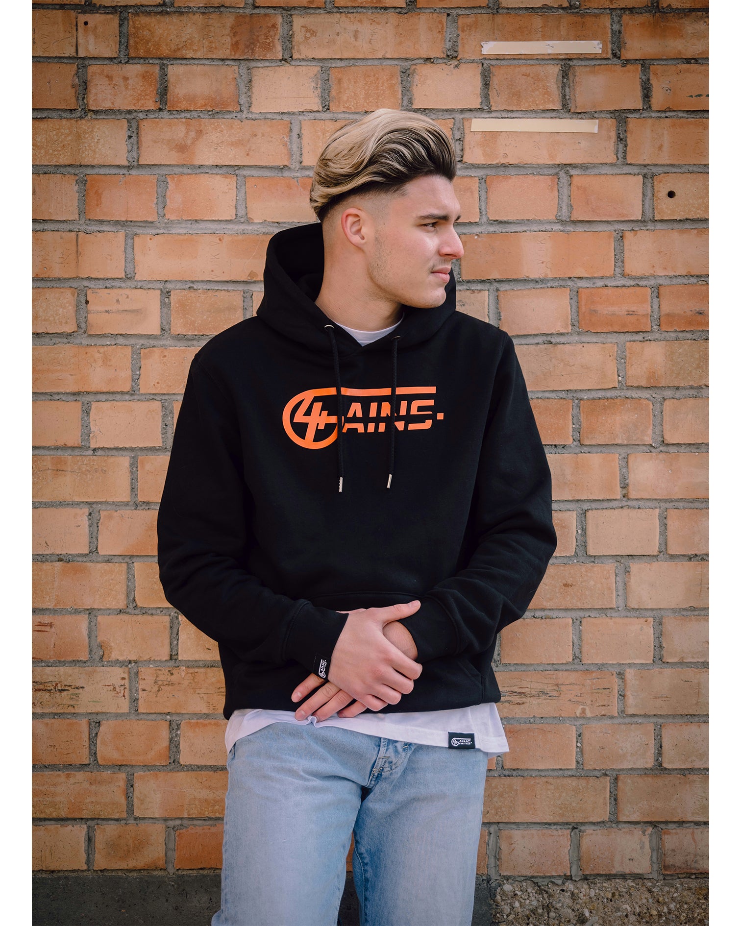 Männliches Model steht an der Wand mit 4GAINS Hoodie in black/orange