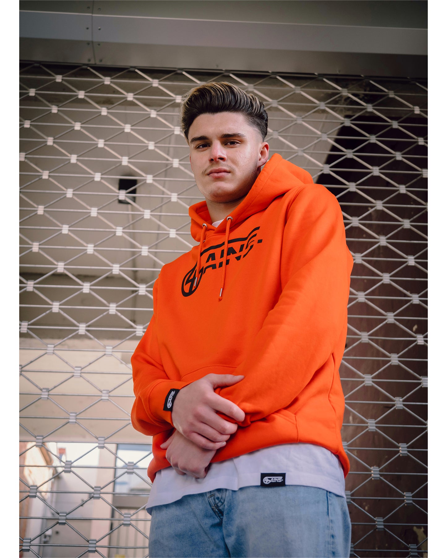 Männliches Model steht mit 4GAINS Hoodie in orange/black