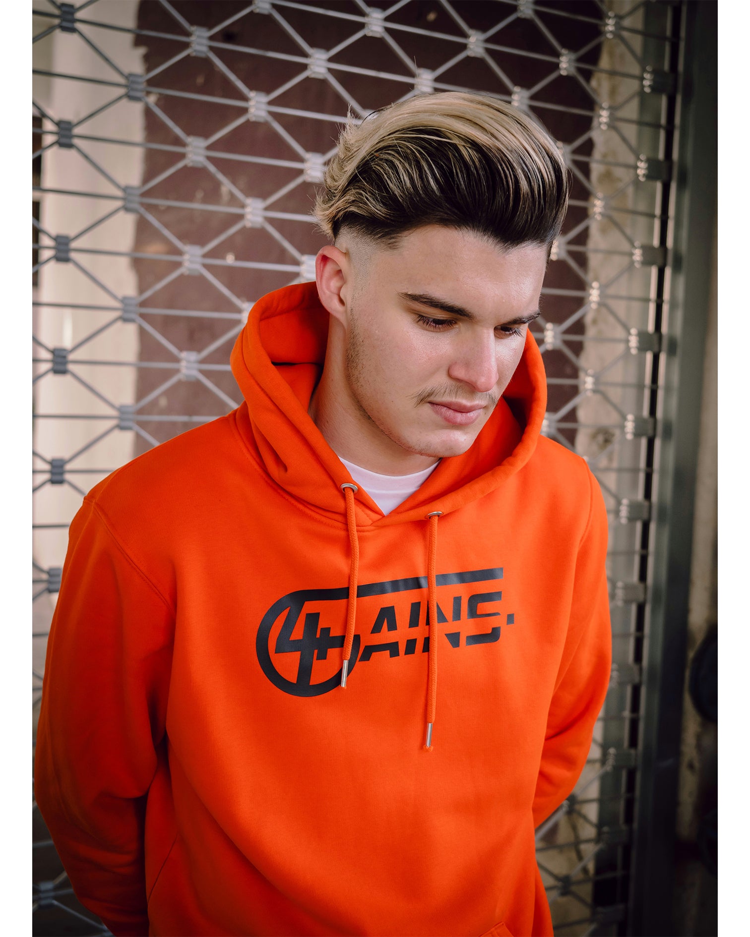 Männliches Model steht mit 4GAINS Hoodie in orange/black