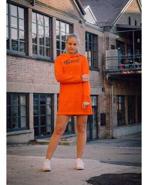 Weibliches Model steht mit weißen Schuhen und dem 4GAINS Sweaterkleid für Frauen in orange/black